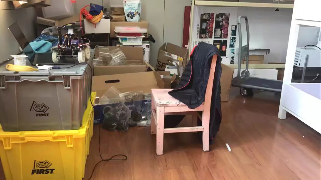 The Rescue Maze robot resting on equipment cases beside a pink stool in the academy workspace where it was developed.